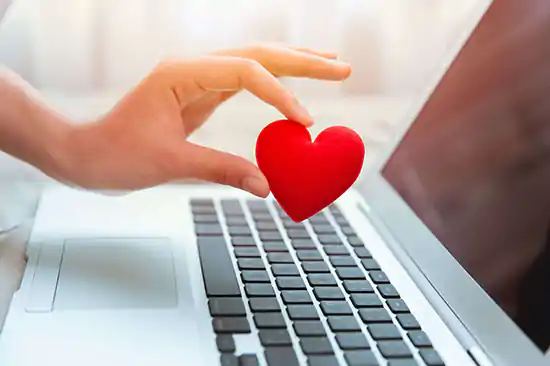 Hand holding red heart over laptop keyboard