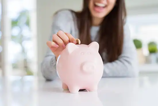 smiling woman in blue sweater inserting coin in piggy bank