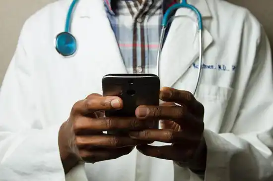 afroamerican in doctors outfit holding phone with both hands 